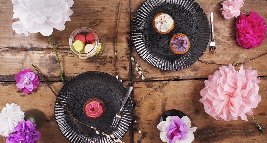 Aufnahme eines Tisches von oben, der mit pinken und roosa Papierblumen und Papptellern geschnmückt ist.