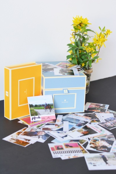 Auf einem Tisch Fotoboxen von Semikolon in blau und gelb, davor Poladroid-Fotos