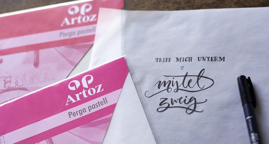 Handgeschriebener Spruch auf Transparentpapier, daneben Verpackung des Transparentpapiers von Artoz