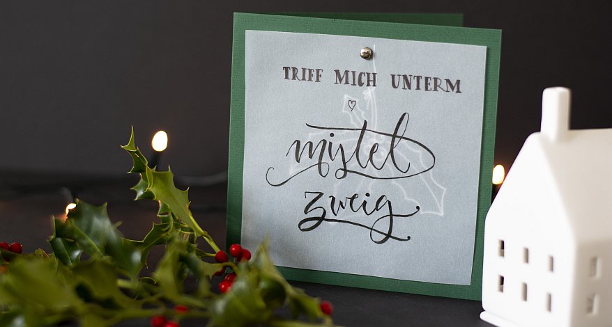 Gebastelte Weihnachtskarte mit Schriftzug „Triff mich unterm Mistelzweig“ in festlicher Dekoration.