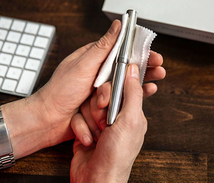 Jemand poliert einen silbernen Füller vor einem Holzschreibtisch mit einem weißen Tuch.