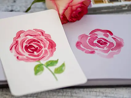 Auf einem cremefarbenen und einem graugetönten Aquarellpapier von Hahnemühle wurde jeweils eine rote Rose aquarelliert. Sie liegen zum Vergleich nebeneinander.