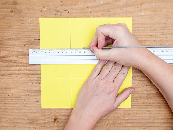 ((Jemand fährt mit einer dünnen Stricknadel entlang eines Lineals Bleistiftlinien auf einen gelben Fotokarton von HEYDA nach. Foto: Johanna Rundel