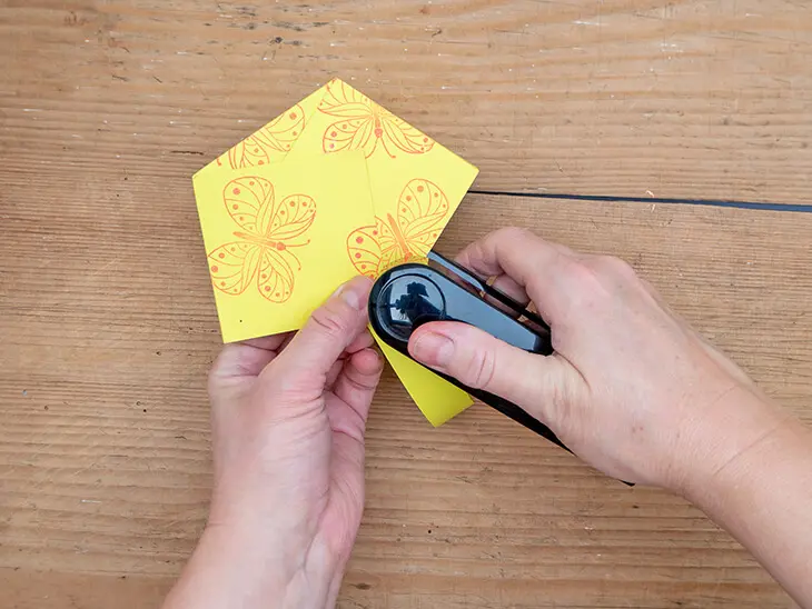 Jemand tackert einen Papierstreifen als Henkel an ein gelbes Osternest aus Papier von HEYDA. Foto: Johanna Rundel