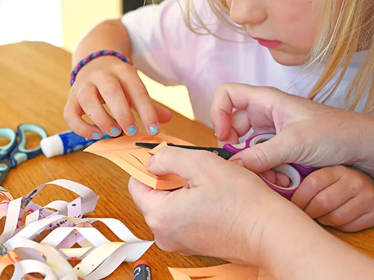 Jemand hilft einem Kind beim Basteln eines Papiersterns mit einer Schere von Pelikan. Foto: Johanna Rundel