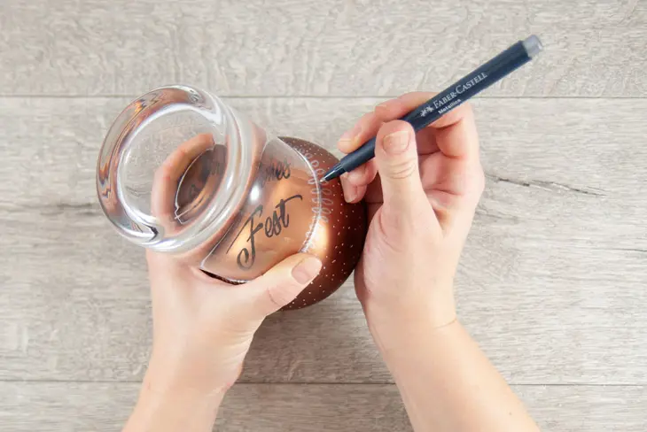 Eine Hand bemalt mit Hilfe eines Metallicmarkers von Faber-Castell eine Weihnachtskugel