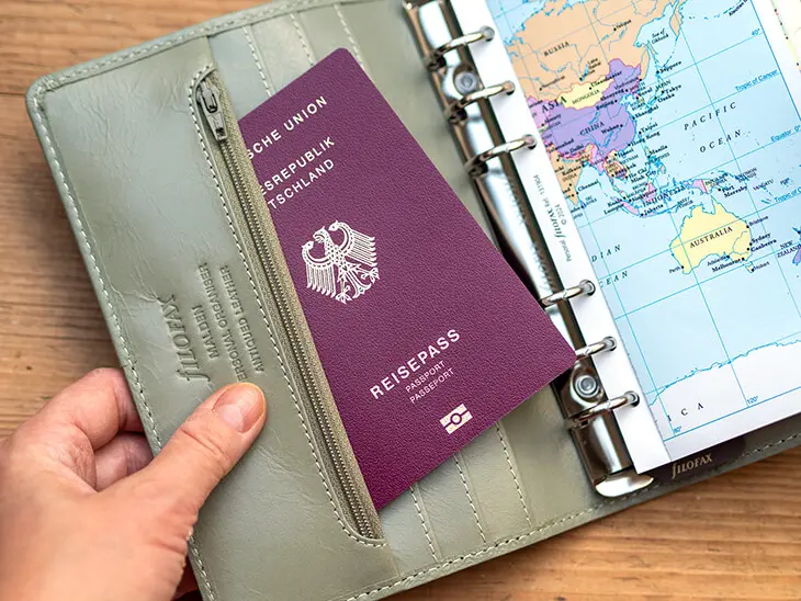 Jemand steckt einen Reisepass in das Innenfach eines grünen Filofax Organizers. Foto: Johanna Rundel