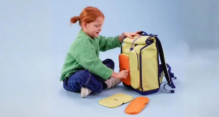 Ein Mädchen sitzt auf dem Boden, vor ihr steht ein gelber Schulranzen von KWIO