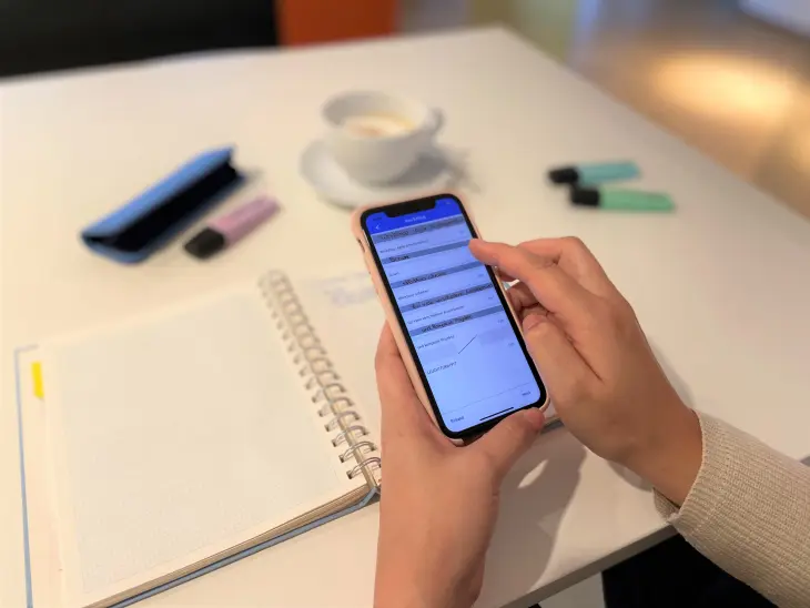 Eine Person nutzt auf ihrem Smartphone die App Pen to Print. Im Hintergrud sieht man einige Schreibutensilien sowie ein aufgeschlagenes Notizbuch.