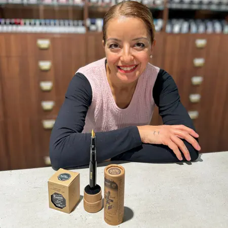 Eine Mitarbeiterin von Ortloff lächelt an einem Tresen, vor ihr befinden sich Tinte und Füllfederhalter.