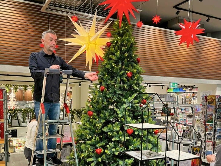Ein Mann steht auf einer Leiter und dekoriert einen Weihnachtsbaum.