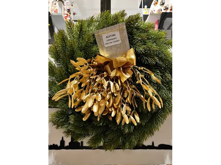 Ein Mistelzweig mit einem Schild "Achtung! Liebespaare bitte hier küssen"
