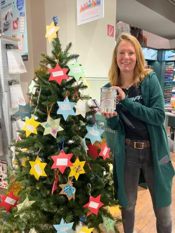Eine Mitarbeiterin steht neben einem mit gebastelten Sternen dekorierten Tannenbaum.sbaum