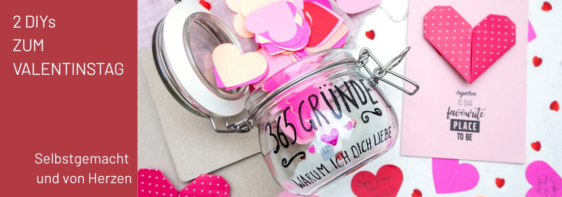 Ein belettertes Einmachglas auf einem Tisch, drumherum liegen rosa und rote Papierherzen und eine gebastelte Karte.