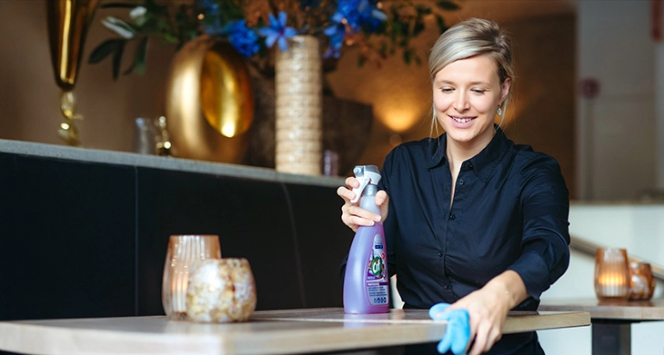 Frau reinigt mit Cif-Reiniger und Mikrofasertuch Tisch in stilvollem Ambiente.