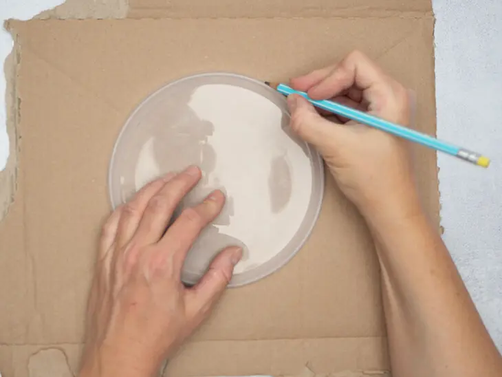Jemand umfährt mit einem Bleistift einen Glasteller auf einem Stück Versandkarton, um den Umriss zu übertragen. Foto: Johanna Rundel