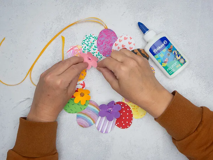 Jemand befestigt mit Bastelkleber von Pelikan bunte DIY-Papierblüten auf einem selbstgebastelten Osterkranz. Foto: Johanna Rundel