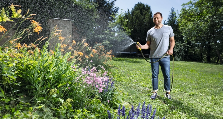 Mann bewässert bunte Blumen mit einem Kärcher Gartenschlauch in einem großen Garten.