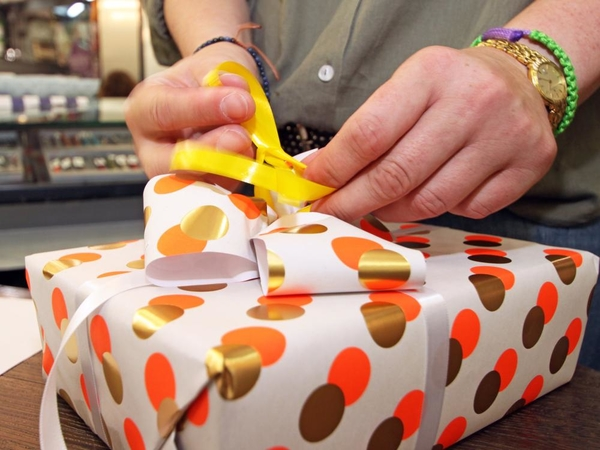 Ein Geschenk wird mit weißen Geschenkpapier mit gold orangenen Punkten verpackt mit eine Schleife.