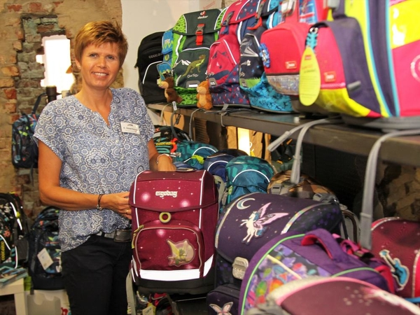 Eine Frau steht neben einer großen Auswahl an Schulranzen.