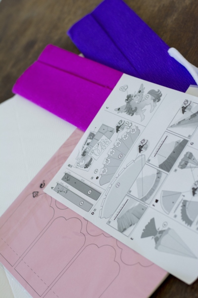 Eine Anleitung aus einem Schultüten Bastel-Set der Marke Heyda liegt auf blauem und pinkem Krepp-Papier.