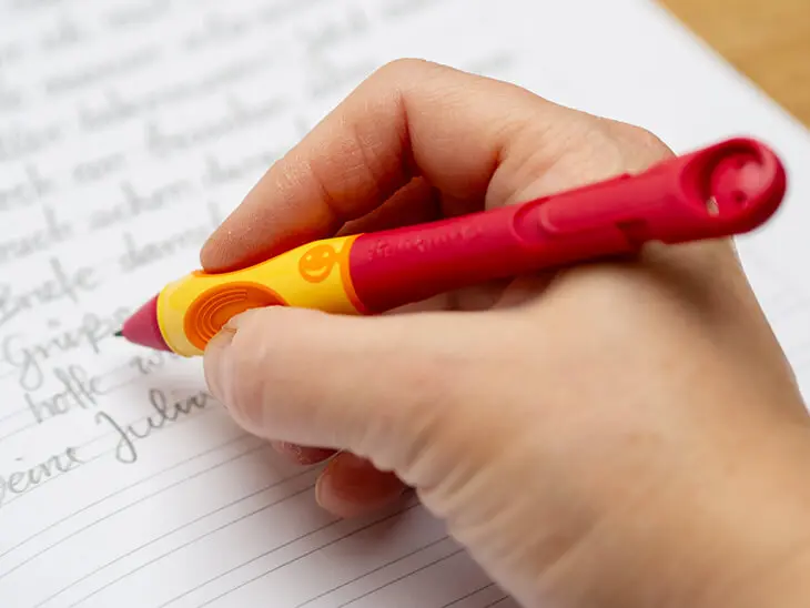 Jemand schreibt mit einem rot-orangenen Schreiblernbleistift von Pelikan einen Brief in ein Heft für die dritte Klasse von herlitz. Foto: Johanna Rundel