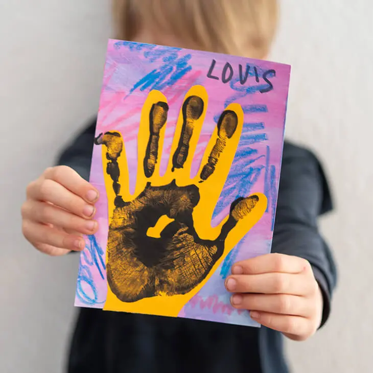Ein Junge im Kindergartenalter hält ein, mit Materialien von STAEDTLER gestaltetes, Kunstwerk mit Handabdruck in die Kamera. Foto: Johanna Rundel