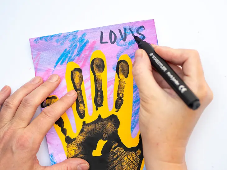 Jemand kritzelt seinen Namen mit einem schwarzen Filzstift von STAEDTLER auf ein Kinderbild. Foto: Johanna Rundel