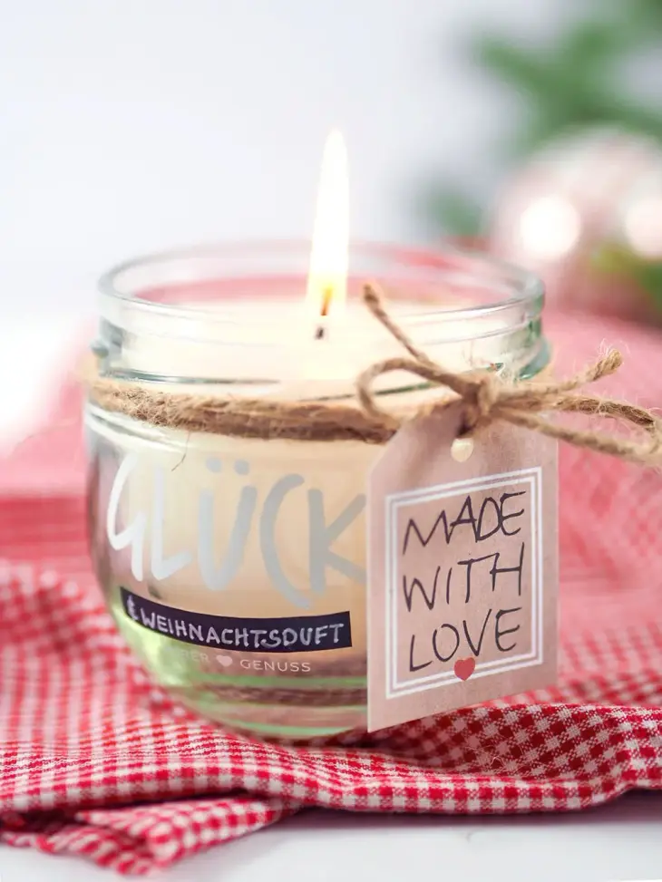 Nahaufnahme einer selbstgemachten Kerze im Glas, weihnachtlich dekoriert und mit einem Anhänger „made with love“)