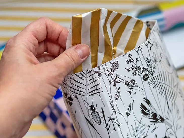 Jemand zieht goldgestreiftes Seidenpapier von STEWO aus einer Geschenktüte. Foto: Johanna Rundel