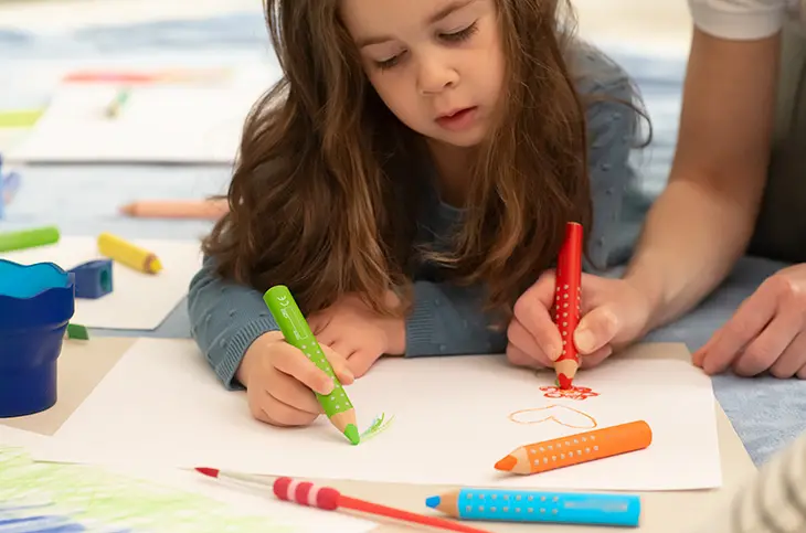 Ein Kind malt konzentriert ein Bild mit dem Buntstift Grippy von Faber-Castell