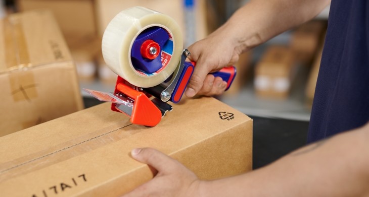 Eine Person verschließt ein Paket mit einem Packbandabroller.
