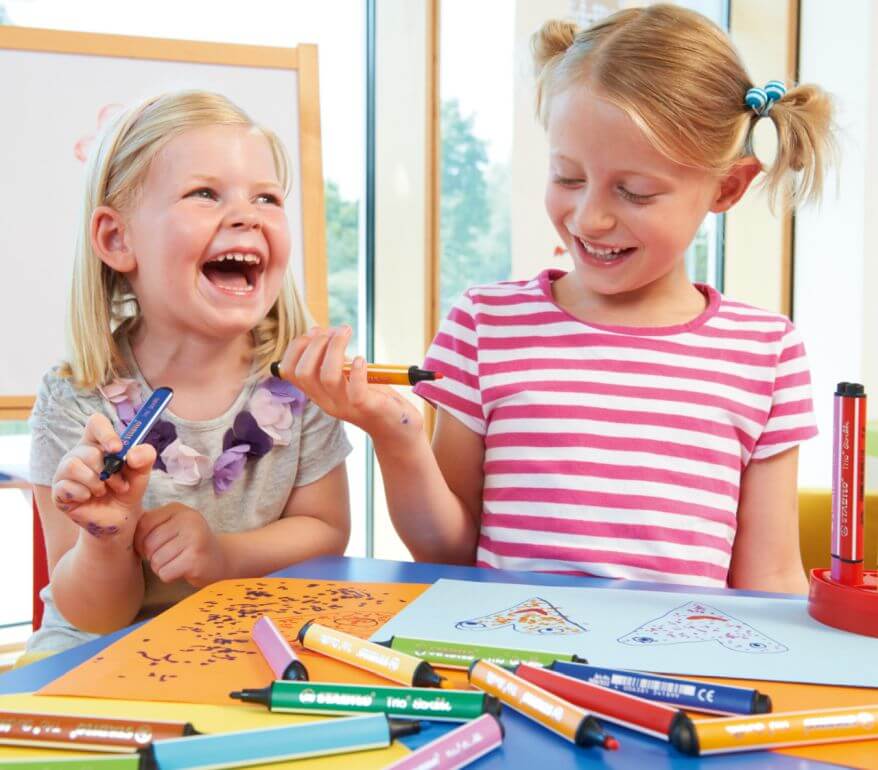 2 kleine Mädchen malen mit bunten Trio Scribbi Filzstiften Bilder und lachen.