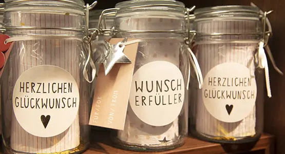 Nahaufnahme dreier kleiner Deko-Weckgläser mit Aufkleber, auf denen "Herzlichen Glückwunsch" und "Wunscherfüller" steht.