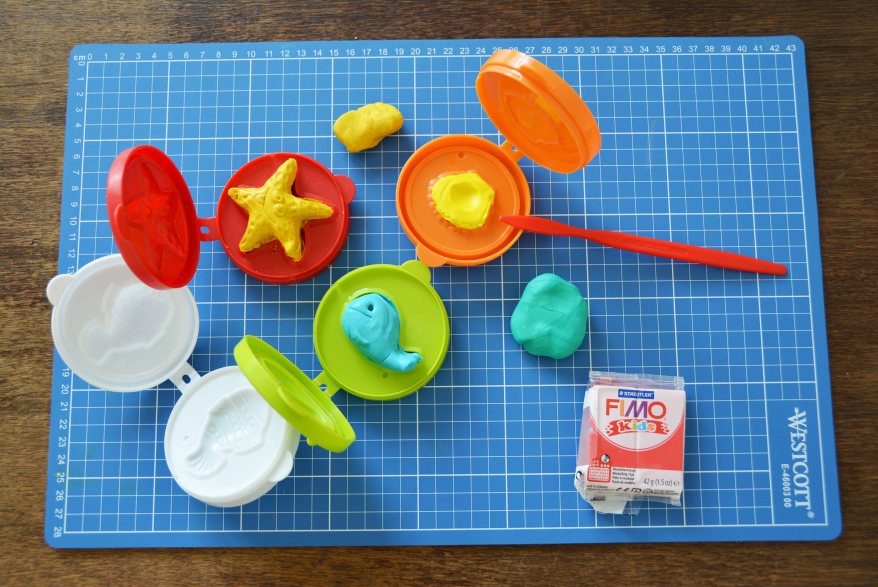 Auf einem Schneidebrett liegen Klappformen aus Plastik, mit denen man Tiere formen kann. In diese ist Fimo gefüllt.