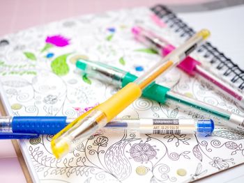 Ein Schülerkalender liegt aufgeschlagen auf einem rosa Untergrund. Es ist ein ZenArt-Motiv zum Ausmalen zu sehen. Darauf Glitzer-Gelstifte von BRUNNEN. Foto: Johanna Rundel