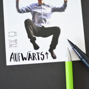 Polariod-Foto mit Aufschrift "es geht aufwärts" und einer springenden Person. Daneben 2 Stifte.