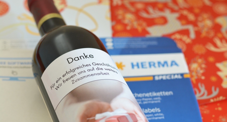 Weinflasche mit Etikett "Danke" liegt auf Geschenkpapier und HERMA Etiketten.