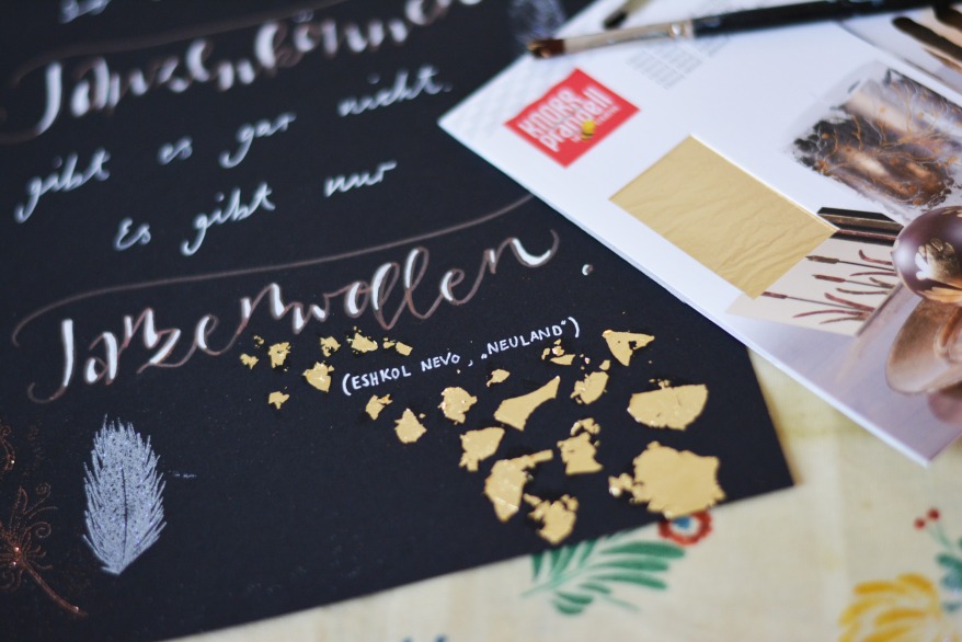 Schwarzes Papier mit Lettering-Zitat und Blattgold, daneben Materialset von Knorr prandell