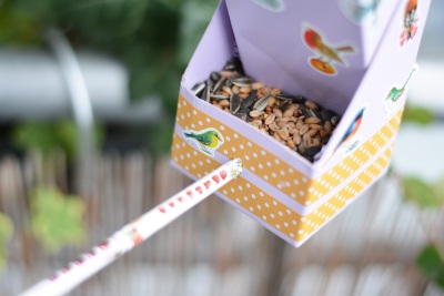 Nahaufnahme des Futterfachs des Vogelhäuschens, welches mit Vogelfutter befüllt ist. In dem Futterfach ist ein Holzstab eingesteckt, auf dem Vögel laden können.