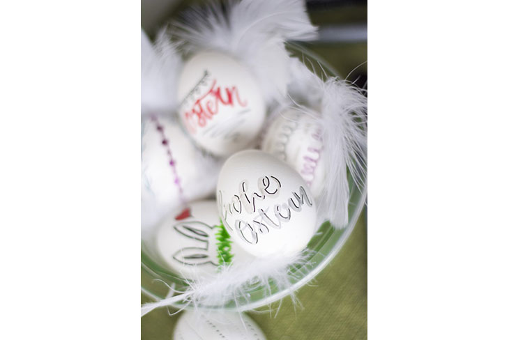 Schale mit beletterten Ostereiern und weißen Federn