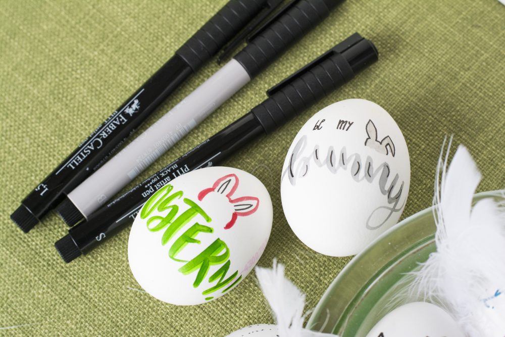Zwei bemalte Ostereier neben Faber-Castell-Stiften auf grünem Stoff