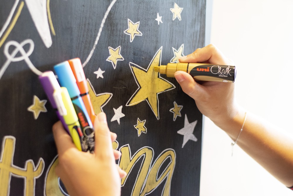 Hände malen gelben Stern mit Kreidestift auf Tafel