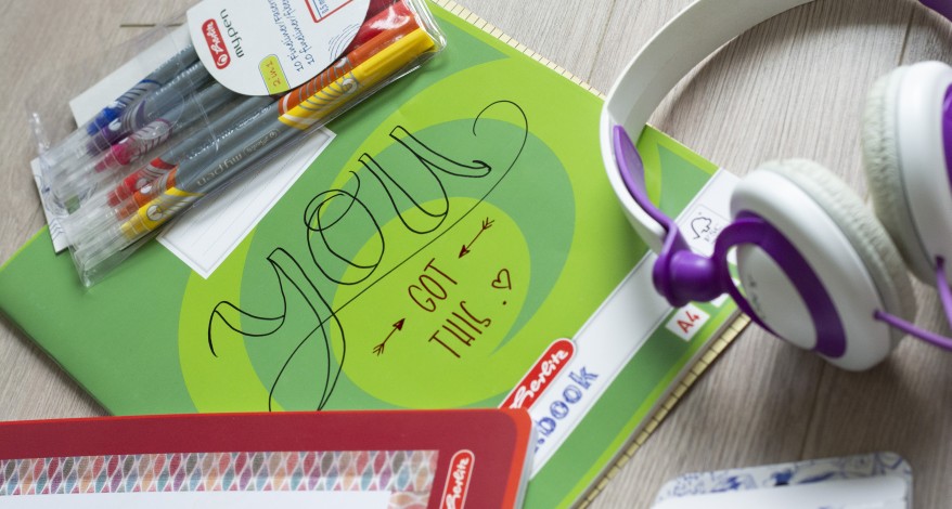 Auf einem hellen Schreibtisch liegen ein weißer Kopfhörer sowie Notizhefte der Marke Herlitz, die mit Hilfe von buntem Klebeband und Finelinern verziert wurden. Es ist ein Lettering mit den Worten "You got this" zu sehen.