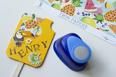 Eine als ein Eis am Stiel gestaltete Einladungskarte wird mit einem Motivstanzer beschnitte. Im Bildrand ist außerdem Twin Papers von Rössler zu sehen.