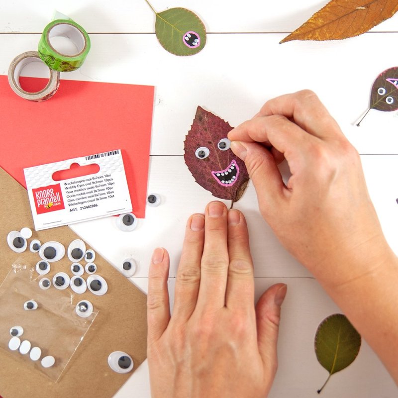 Wackelaugen werden auf ein rotes Blatt für Herbstkarte geklebt