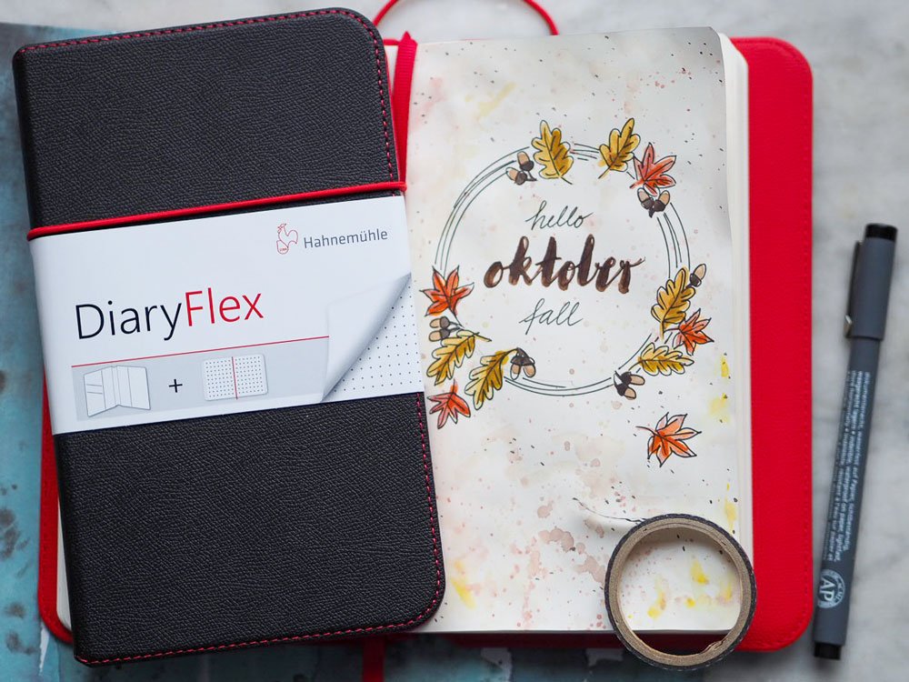 Ein geschlossenes Bullet Journal und eine beletterte Seite mit Herbstmotiv eines Bullet Journals auf einem Tisch.