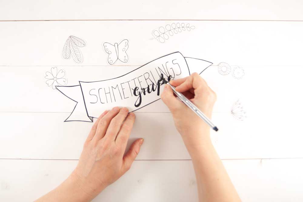 Hand schreibt „Schmetterlingsgrüße“ auf Papierbanner