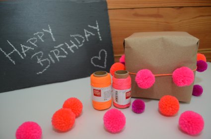 Verpacktes Geschenk mit pinken Pompons als Dekoelement.