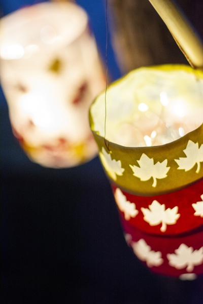 Nahaufnahme leuchtender Laterne mit roten und gelben Ahornblättern an einem Ast in der Dunkelheit.